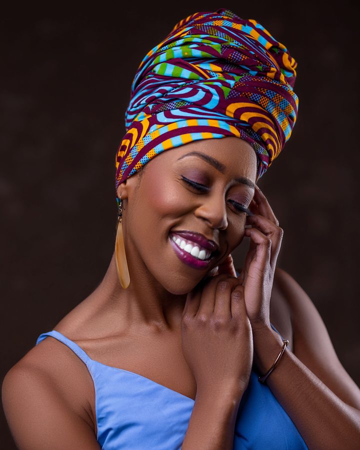 Femme souriante, yeux fermés, coiffée d'un foulard à motifs noué en turban