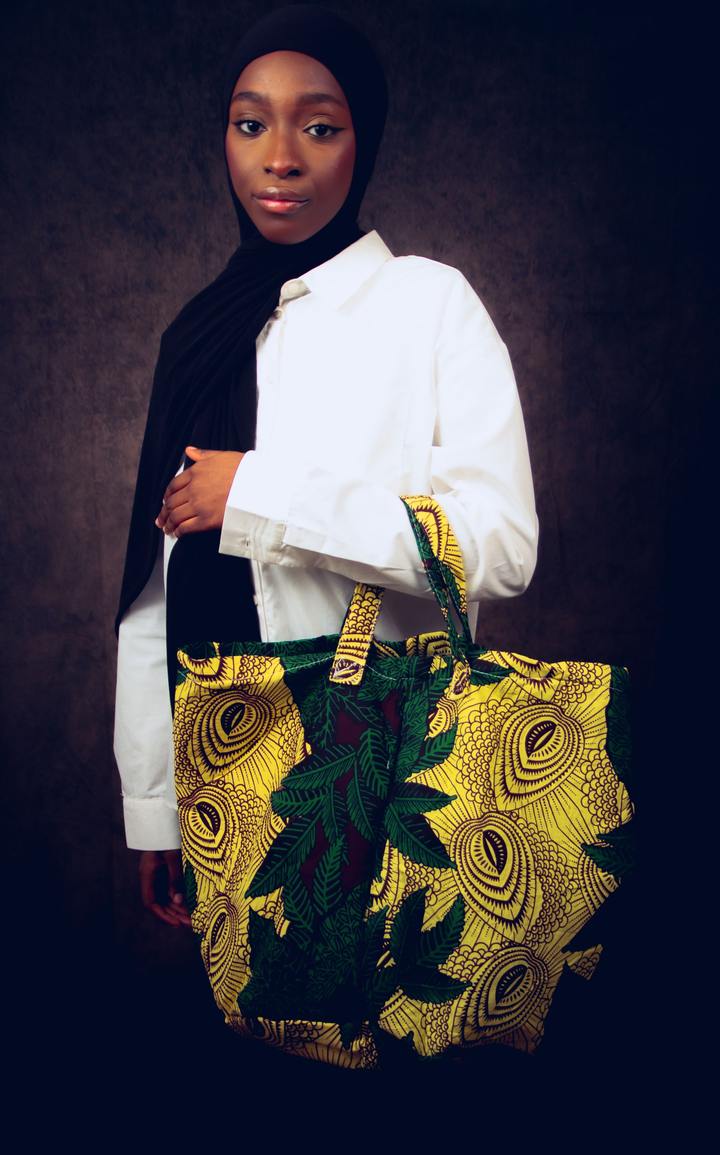 Femme en chemise blanche tenant un grand sac cabas en wax jaune et vert