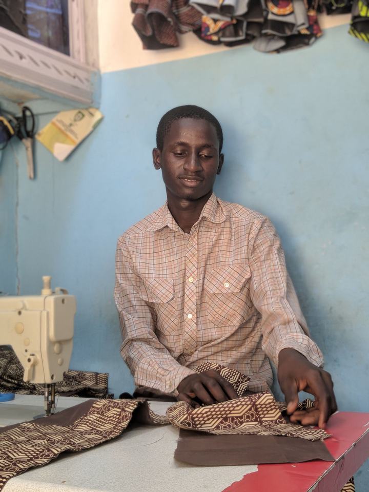 Tailleur souriant assis devant sa machine à coudre, travaillant un tissu wax brun et beige