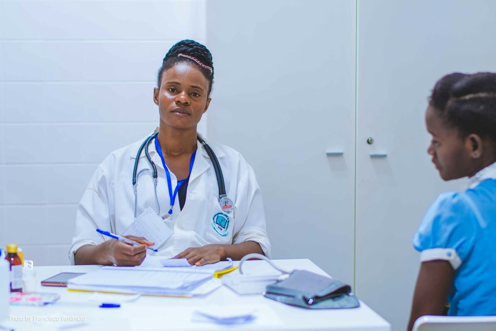 Médecin en blouse blanche, stéthoscope autour du cou, prenant des notes face à une jeune patiente pendant une consultation