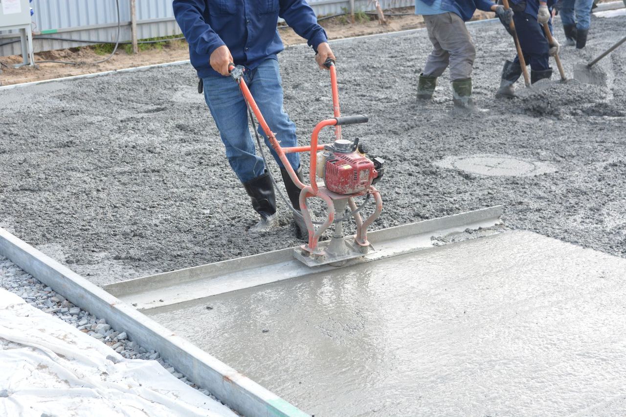 Ouvriers lissant une dalle de béton frais à la règle vibrante