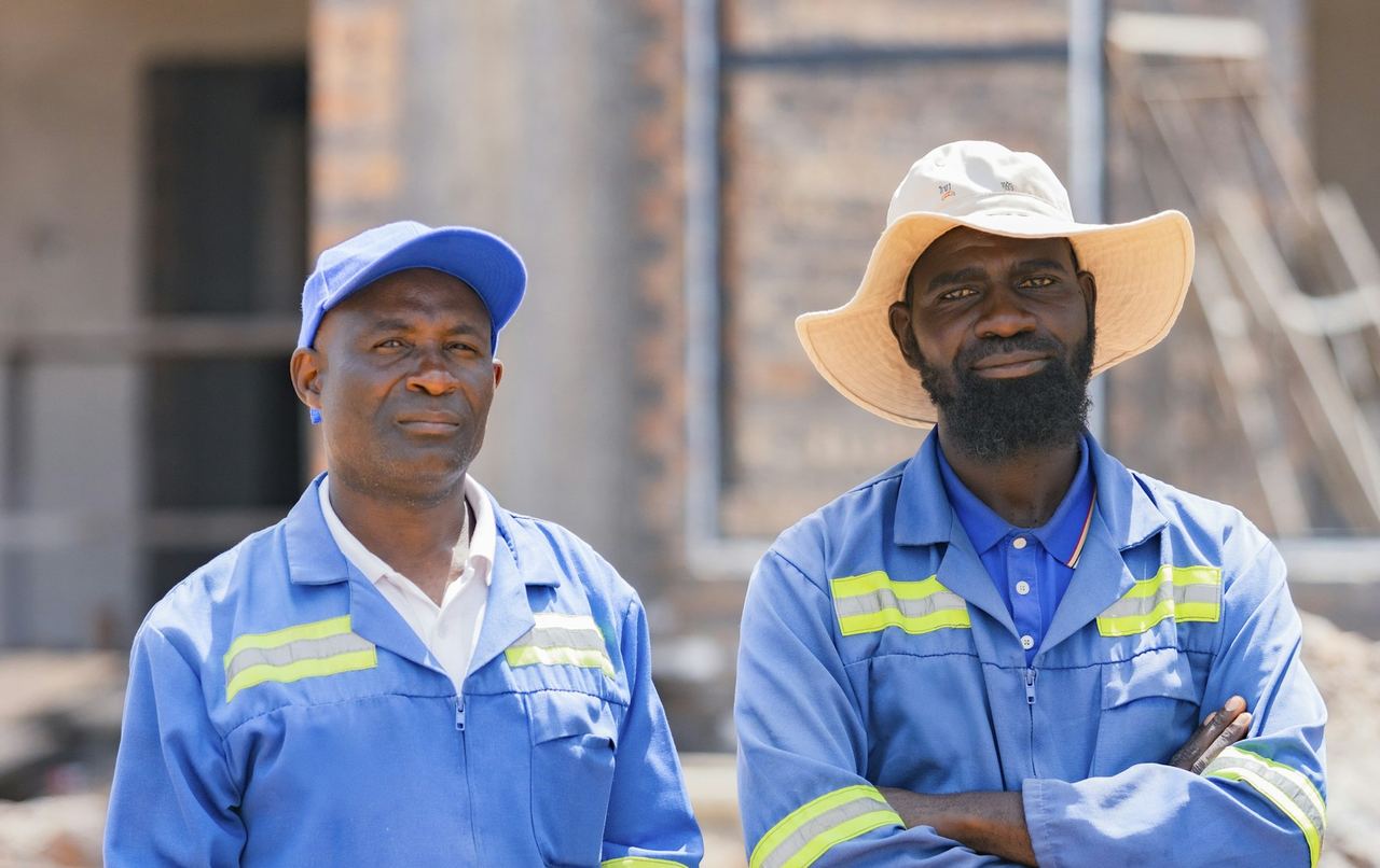 Deux responsables de chantier en tenue de travail bleue, bras croisés, devant un bâtiment en briques en cours de construction