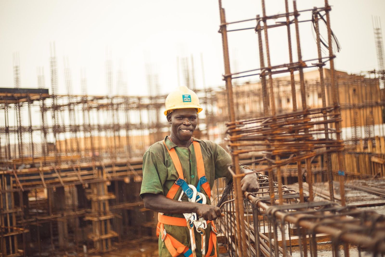 Ouvrier souriant en casque jaune et harnais de sécurité, au milieu des armatures métalliques d'un bâtiment en construction