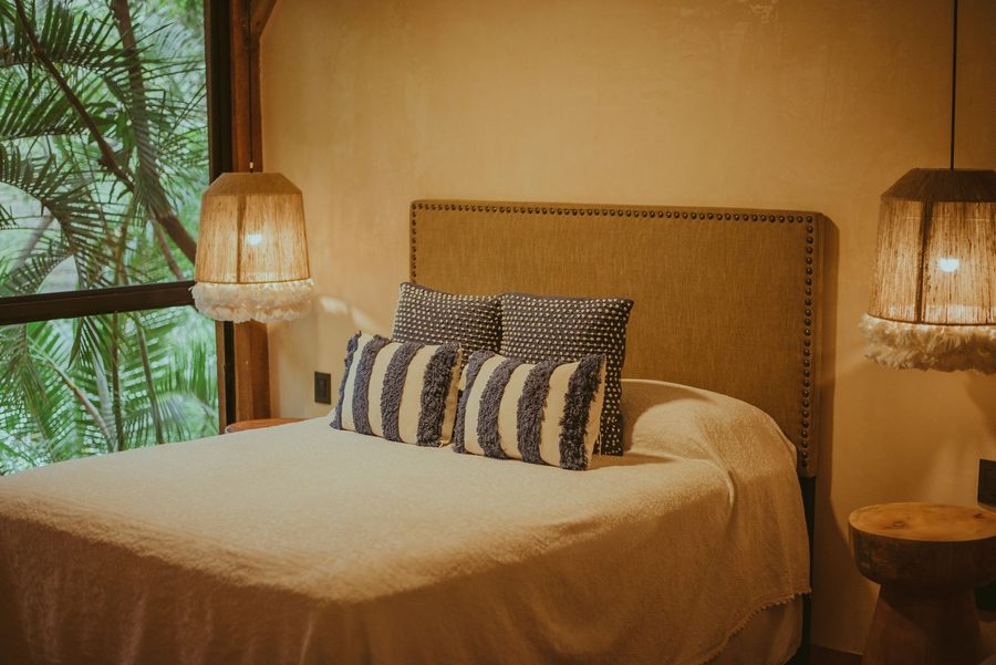 Chambre aux tons chauds avec lit double, lampe en fibres tressées et grande baie ouverte sur les palmiers