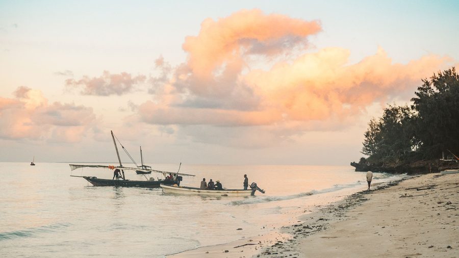 Plage calme au coucher du soleil, avec un bateau traditionnel et des pêcheurs au loin