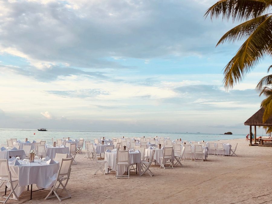 Tables nappées de blanc dressées sur le sable pour une réception en bord de mer