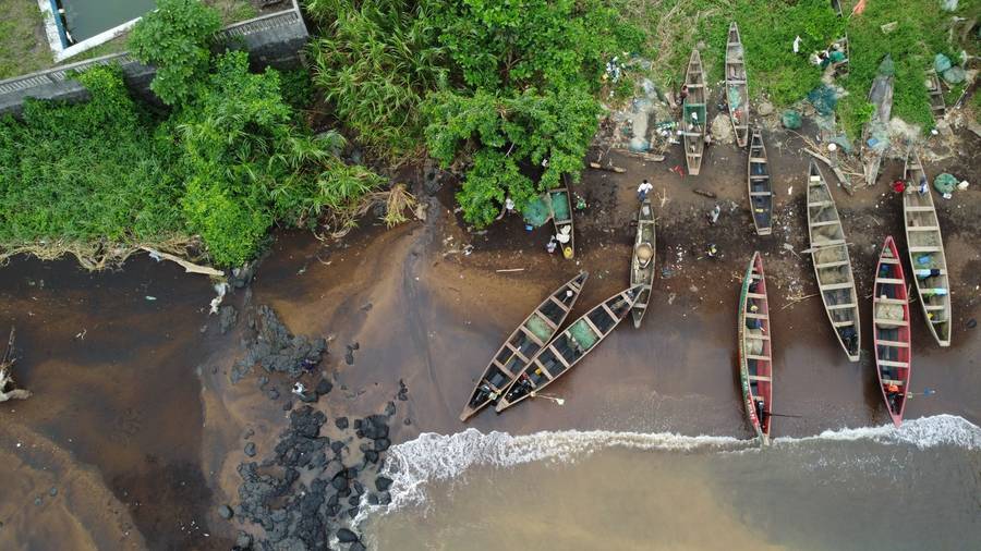 Vue aérienne de longues pirogues de pêche alignées sur une plage de sable sombre au Cameroun