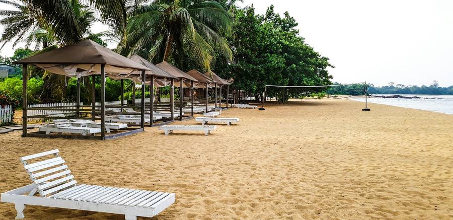 Plage de sable doré de Kribi bordée d'arbres, avec transats blancs et paillotes face à la mer