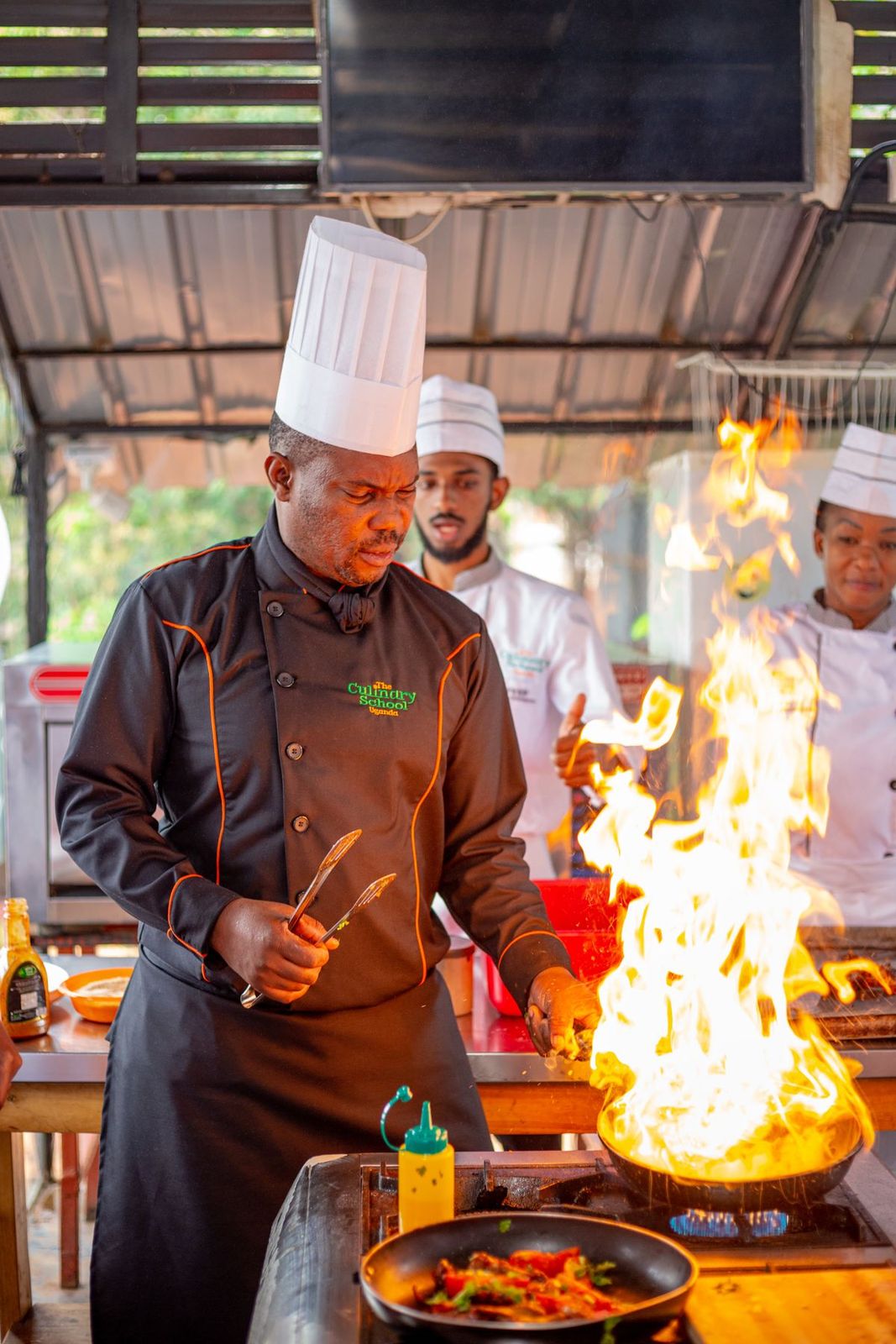 Cuisiniers en tenue blanche préparant des plats au-dessus de hautes flammes