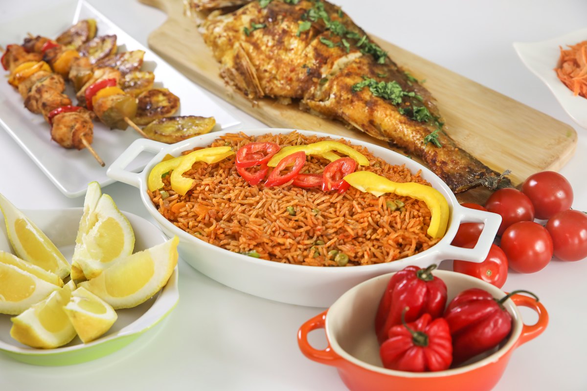 Riz à la tomate servi avec poisson grillé, brochettes, citron et légumes frais