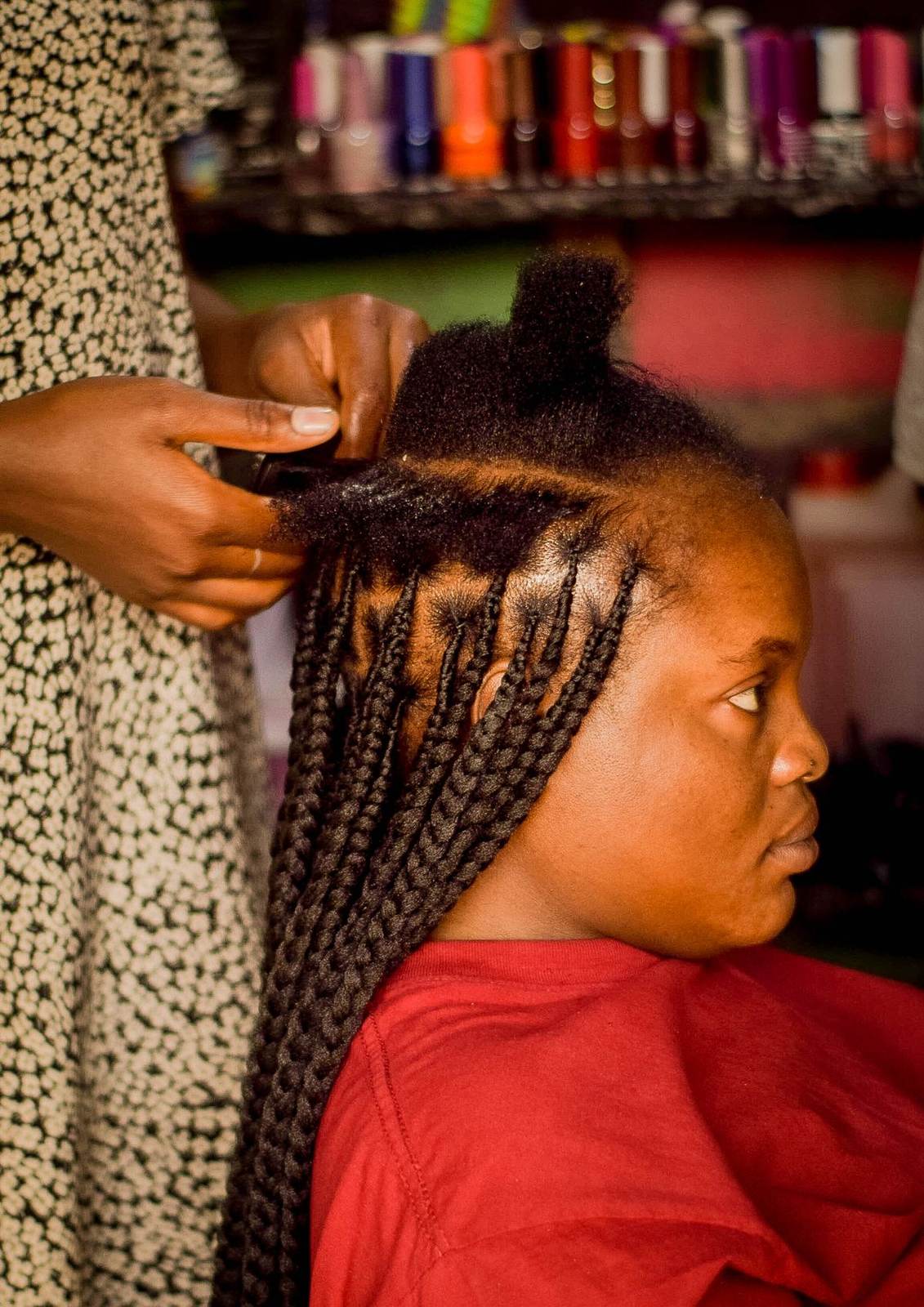 Coiffeuse réalisant de longues tresses sur une cliente dans un salon coloré