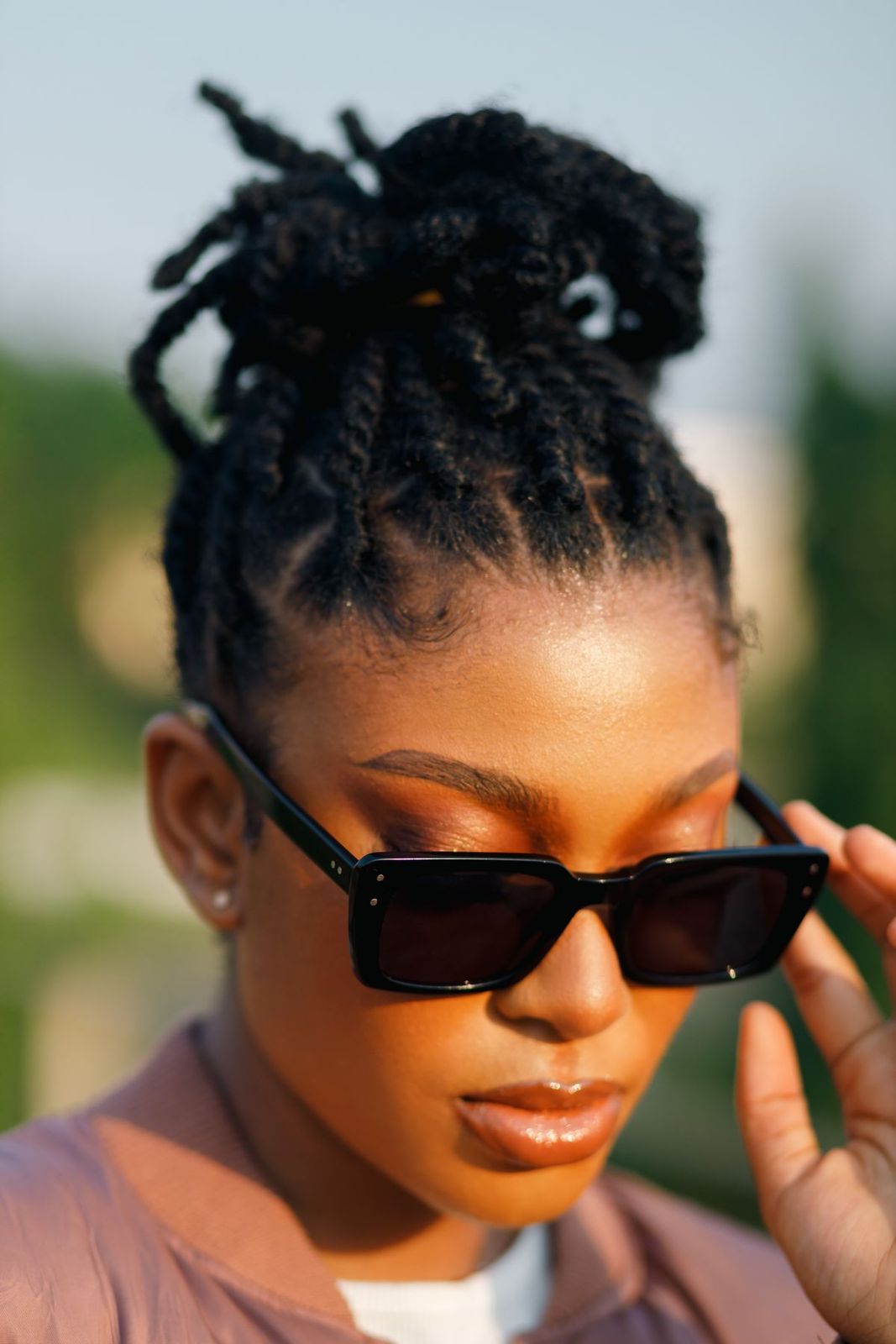 Femme aux locks relevées en chignon, portant des lunettes de soleil