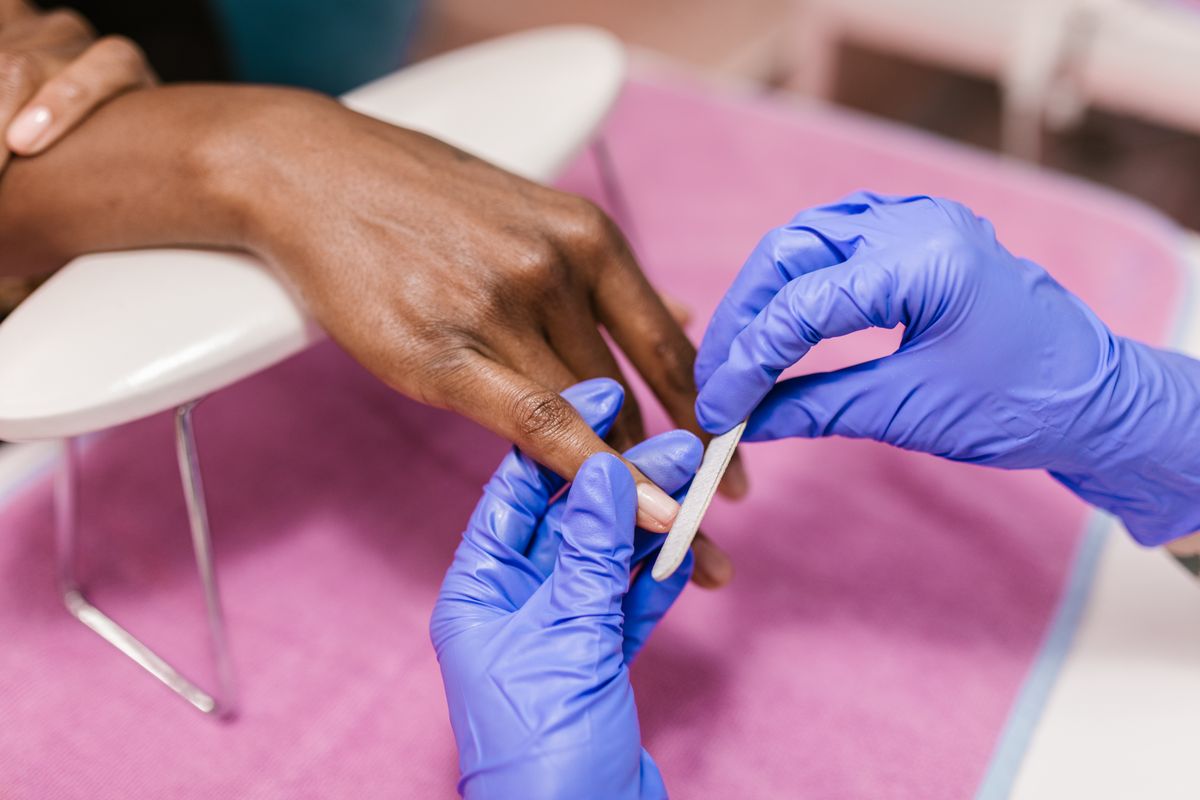 Manucure en cours, mains gantées sur fond rose