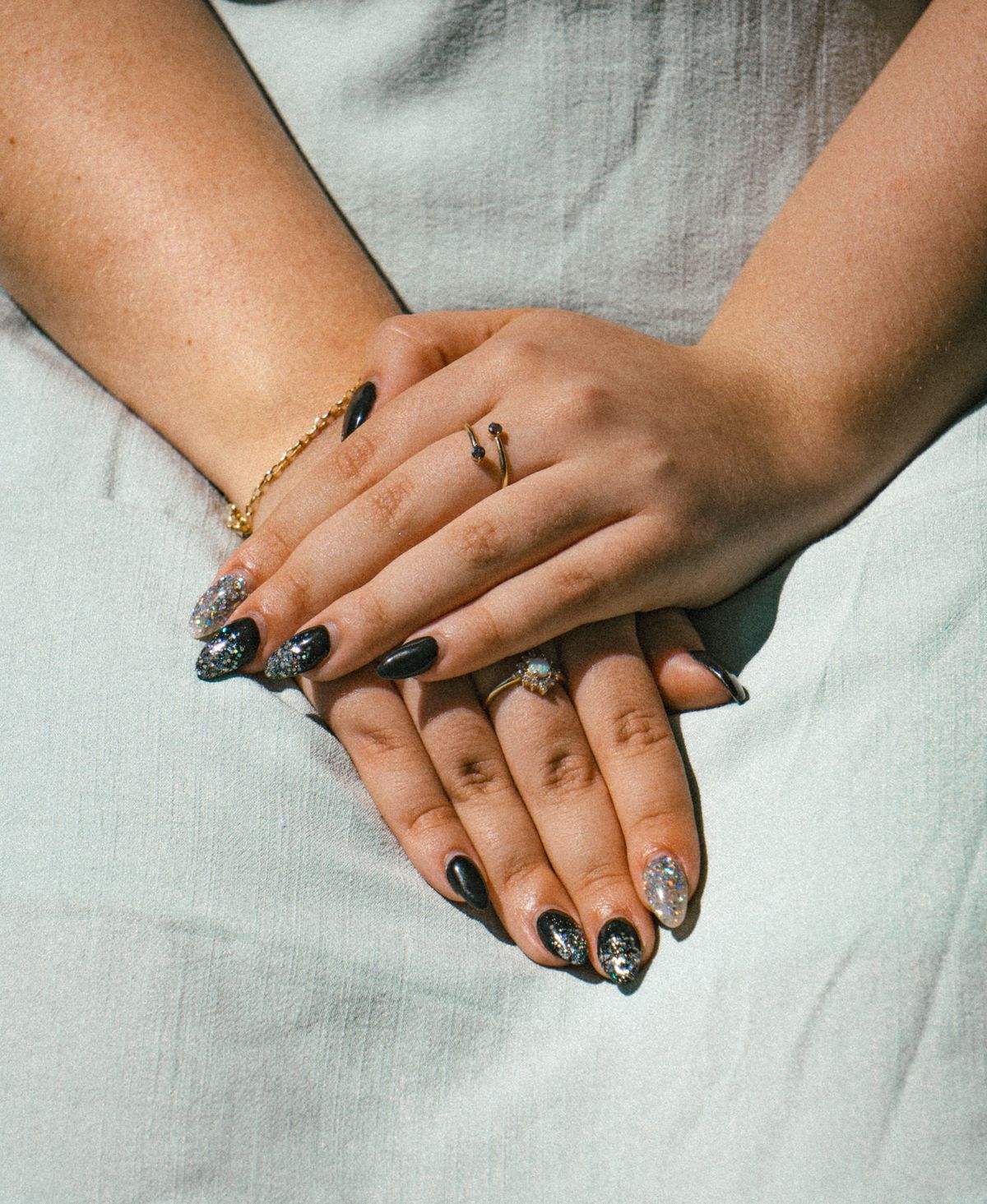 Mains aux ongles vernis noir et argent, ornées de bagues