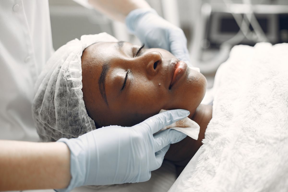 Femme allongée recevant un soin du visage par une esthéticienne gantée